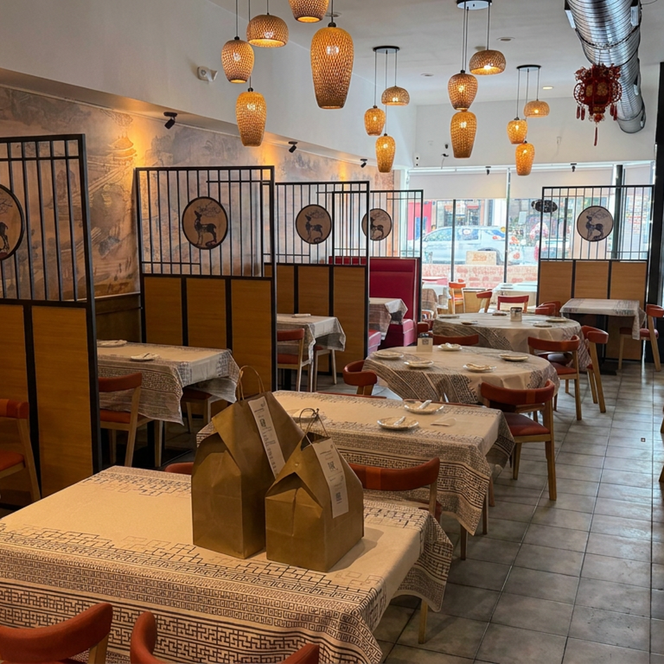 Warmly lit Asian restaurant dining room with patterned tablecloths, red chairs, hanging lanterns, and decorative screens.